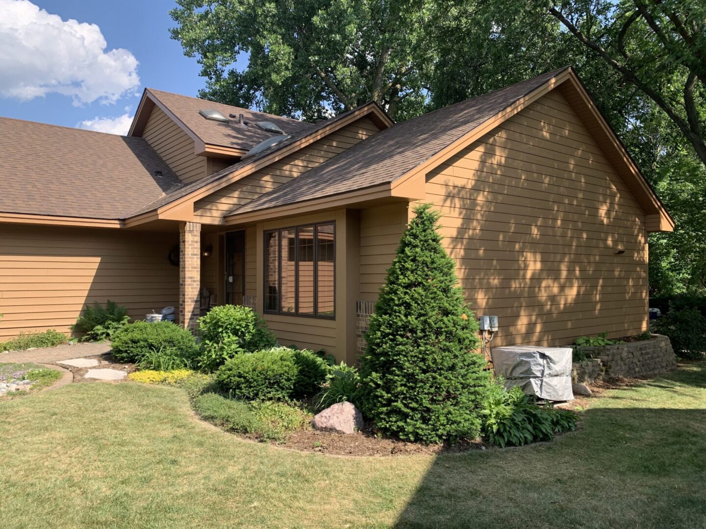 A brown house with bushes and trees in front of it.